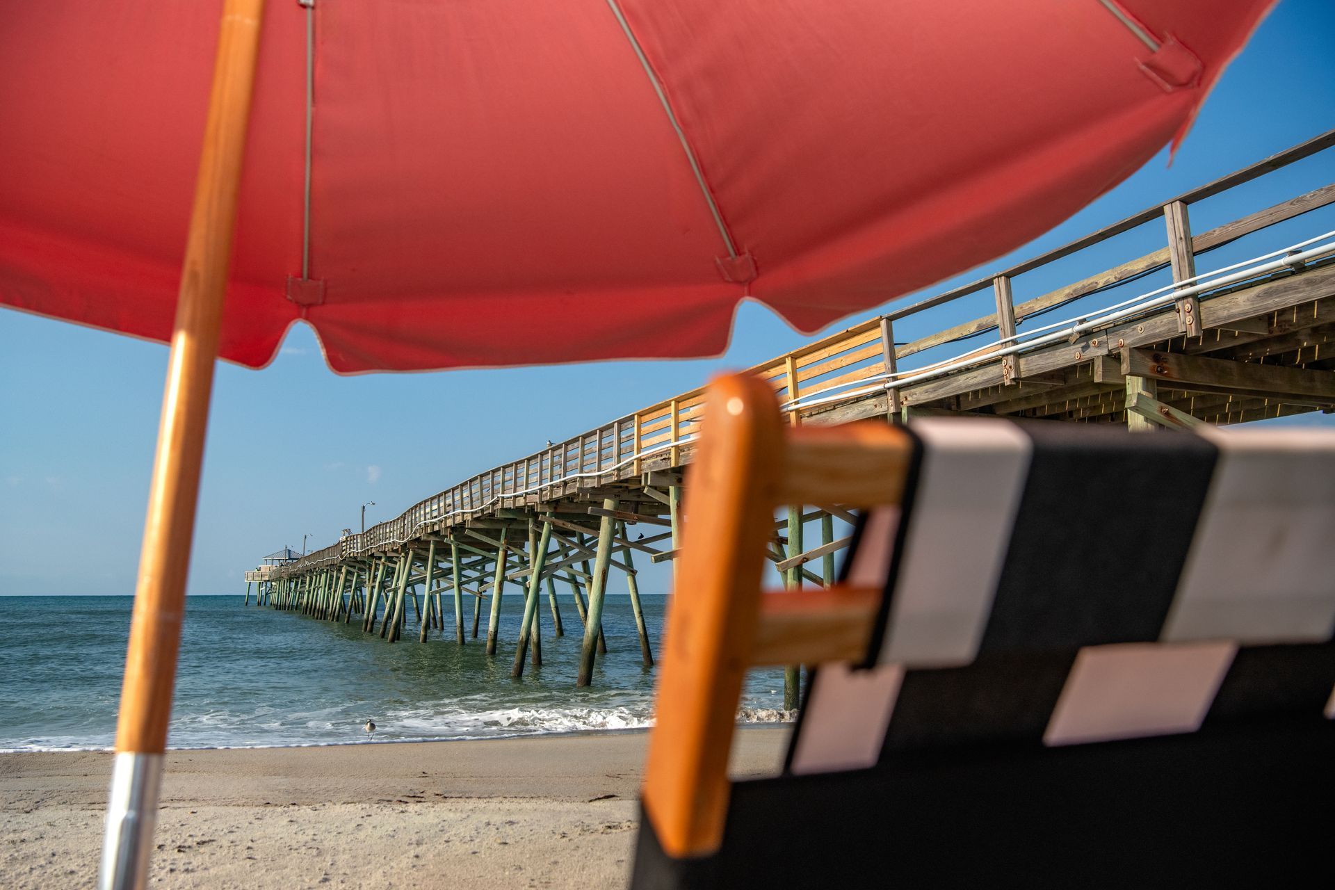 Beach scene with red umbrella and pier extending into the ocean