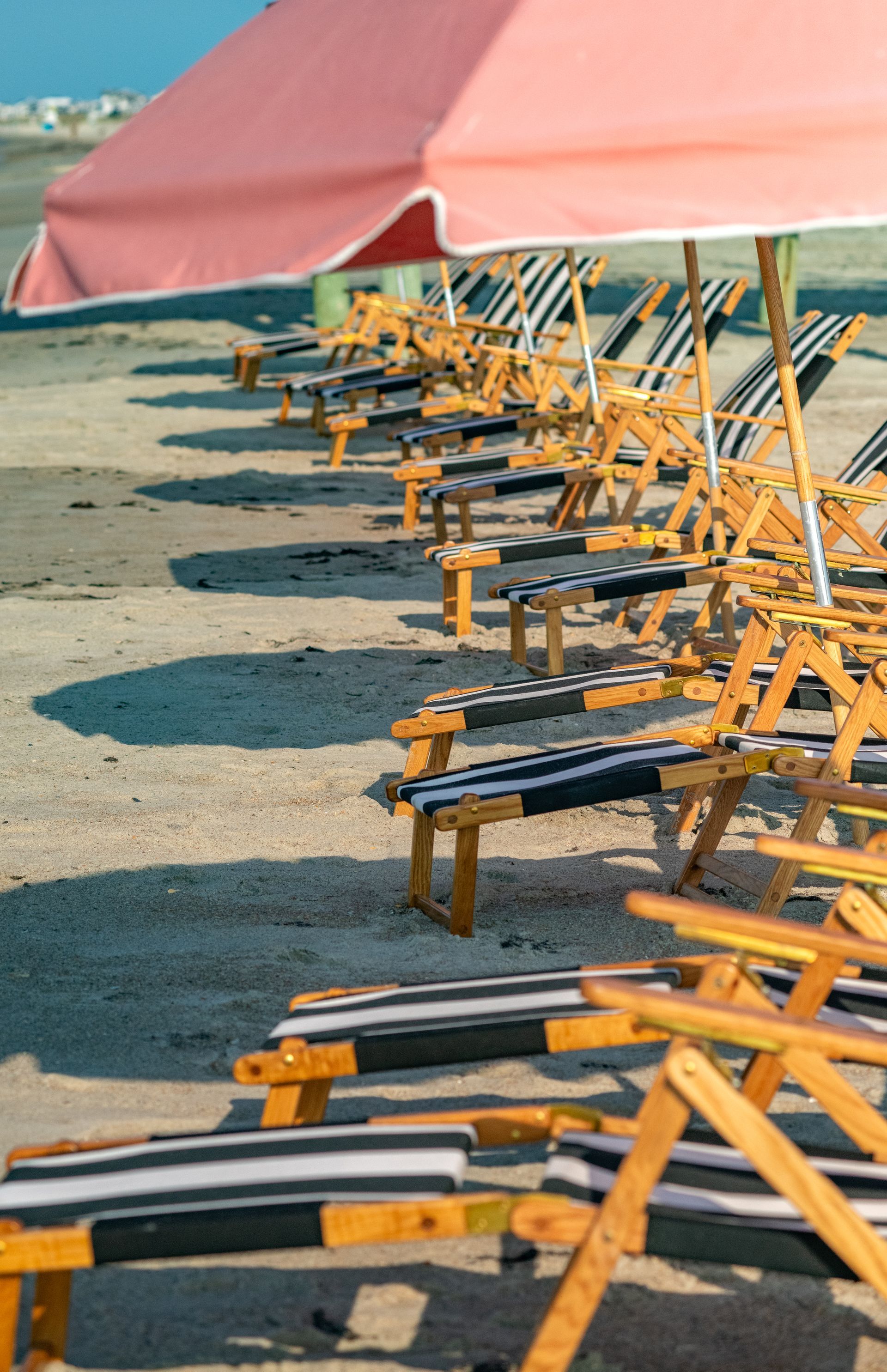 Empty yellow beach chairs lined up under a pink canopy on a sandy beach