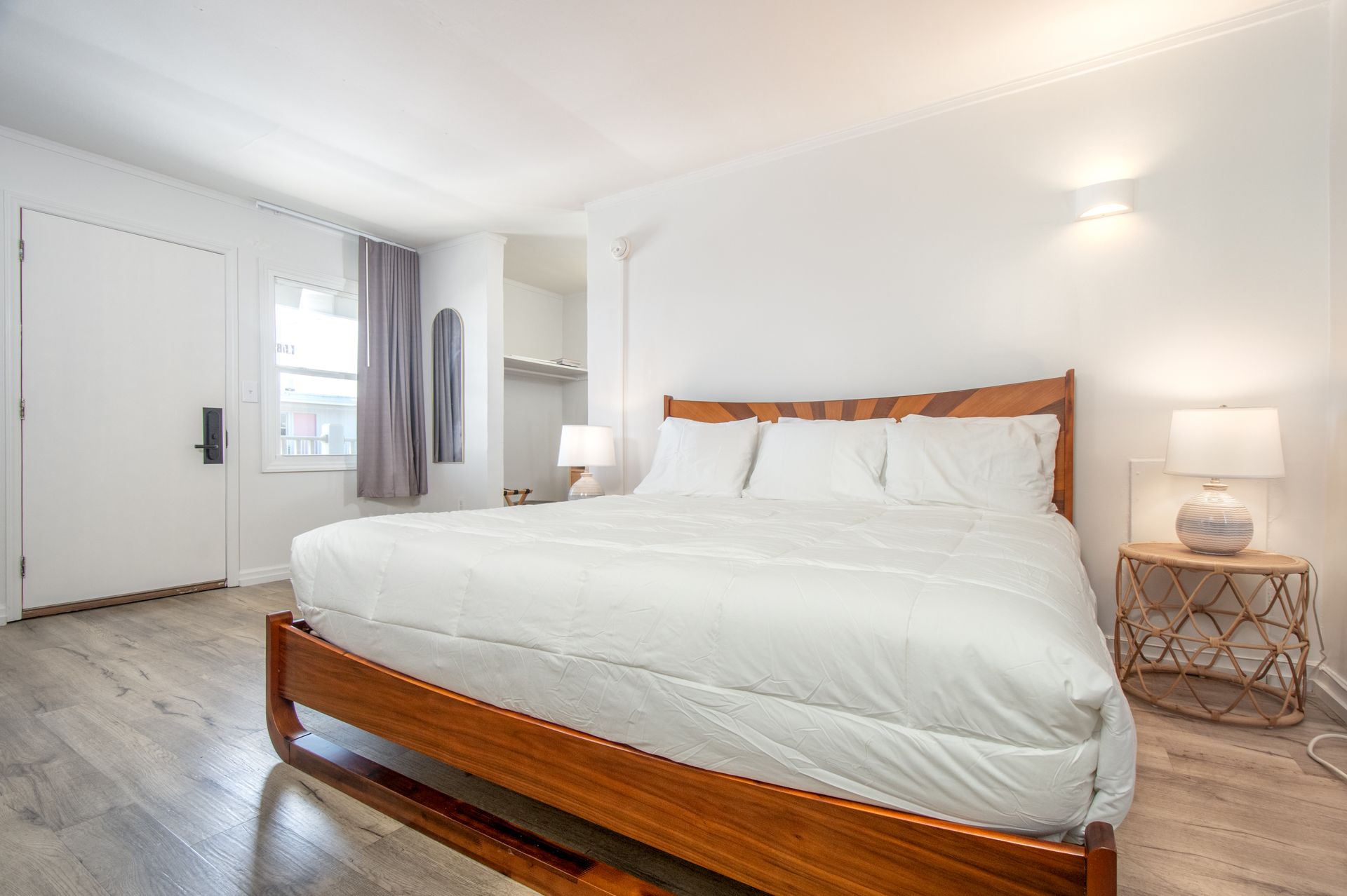 Bright white bedroom with wooden bed frame, bedside lamps, and a closet by the door