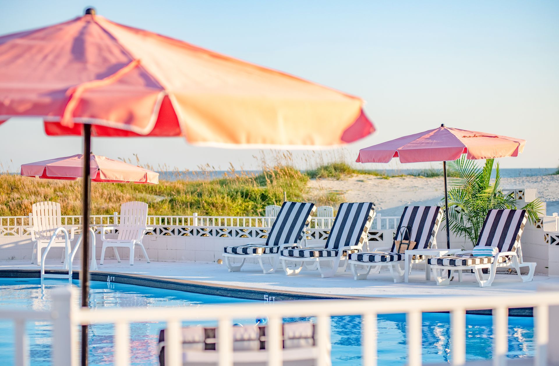 Poolside lounge chairs under pink umbrellas beside a bright outdoor pool.