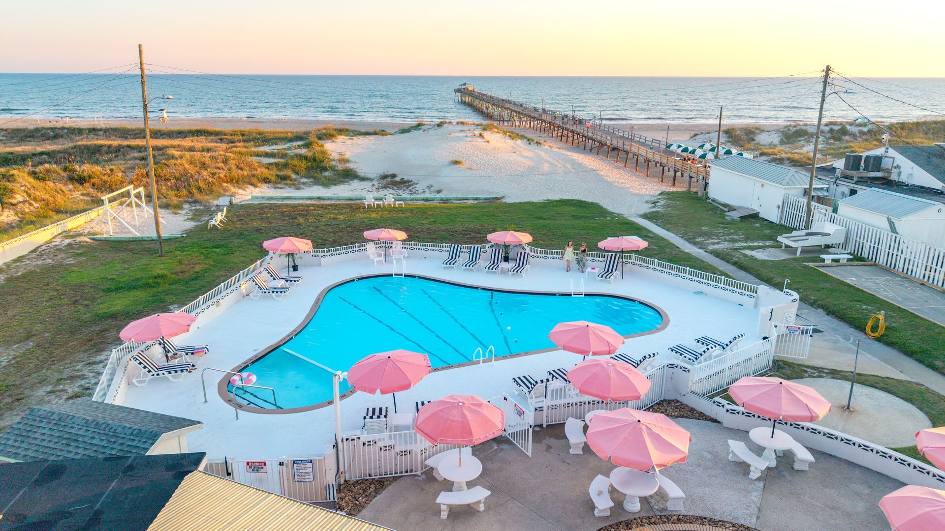 Pink umbrellas around a blue pool by the beach at sunset