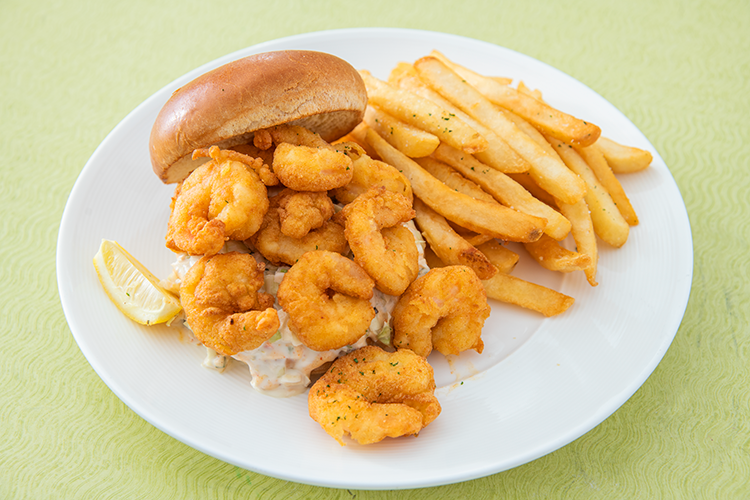 Plate of fried shrimp, fries, and a lemon wedge with a sandwich roll on a green tablecloth