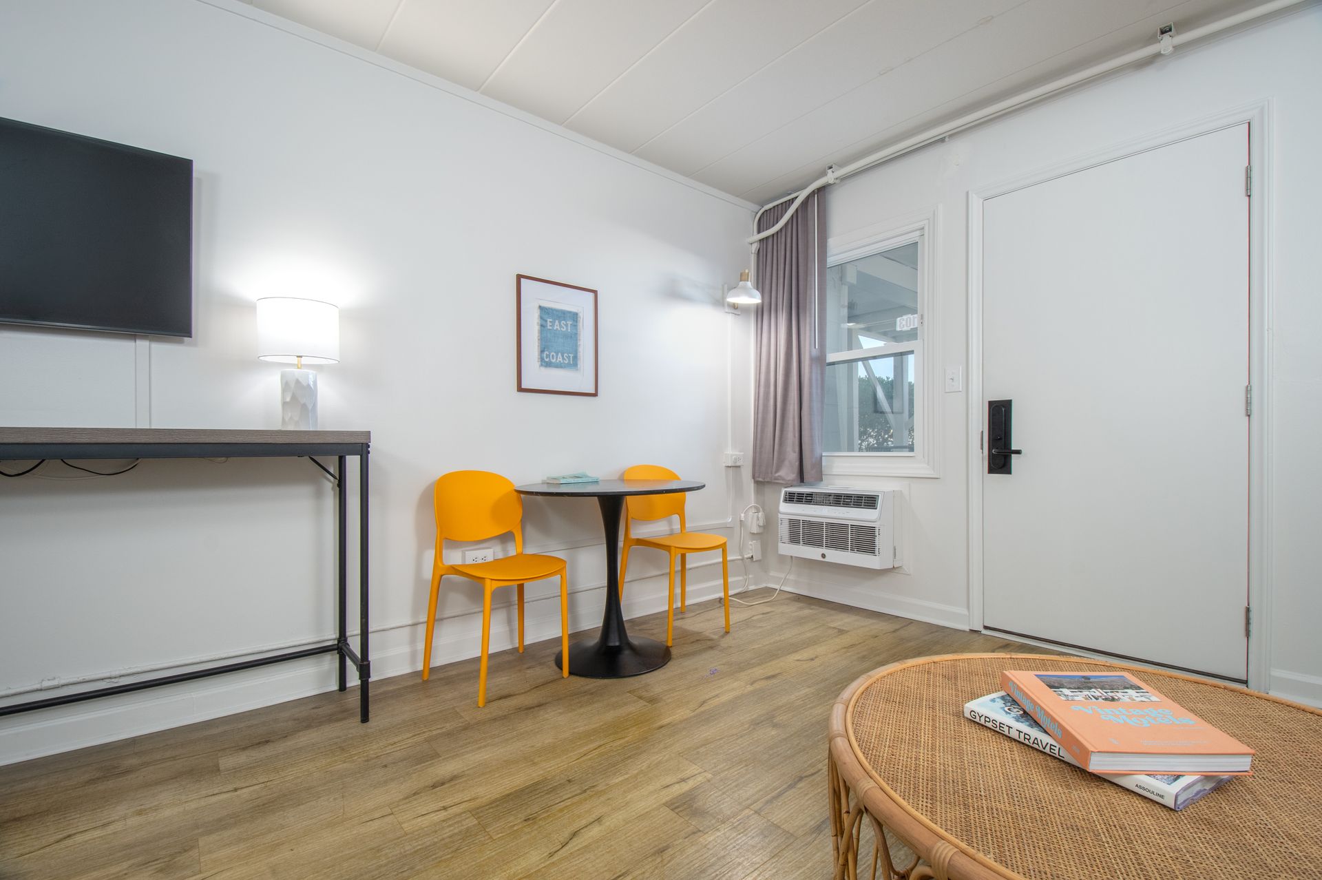 Bright minimalist room with yellow chairs, small table, wall art, and a TV on a console.