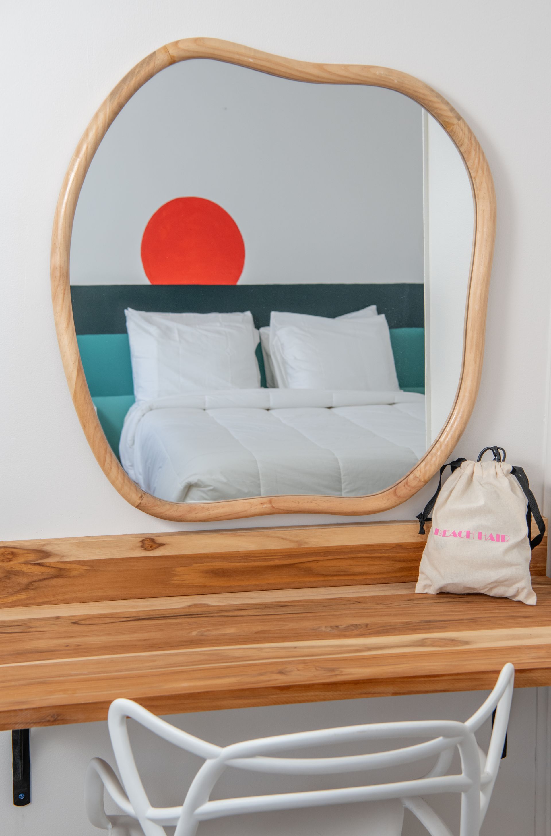 Round mirror above desk reflects bed and red wall art in a hotel room.