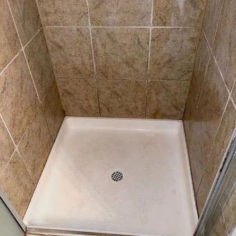 Empty beige shower stall with white base and center drain.