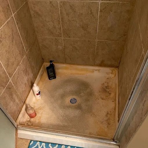 Tiled shower stall with a dirty floor, drain, and two bottles in the corner