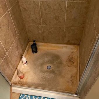 Small tiled shower stall with a dirty floor, drain, and shampoo bottles in the corner.