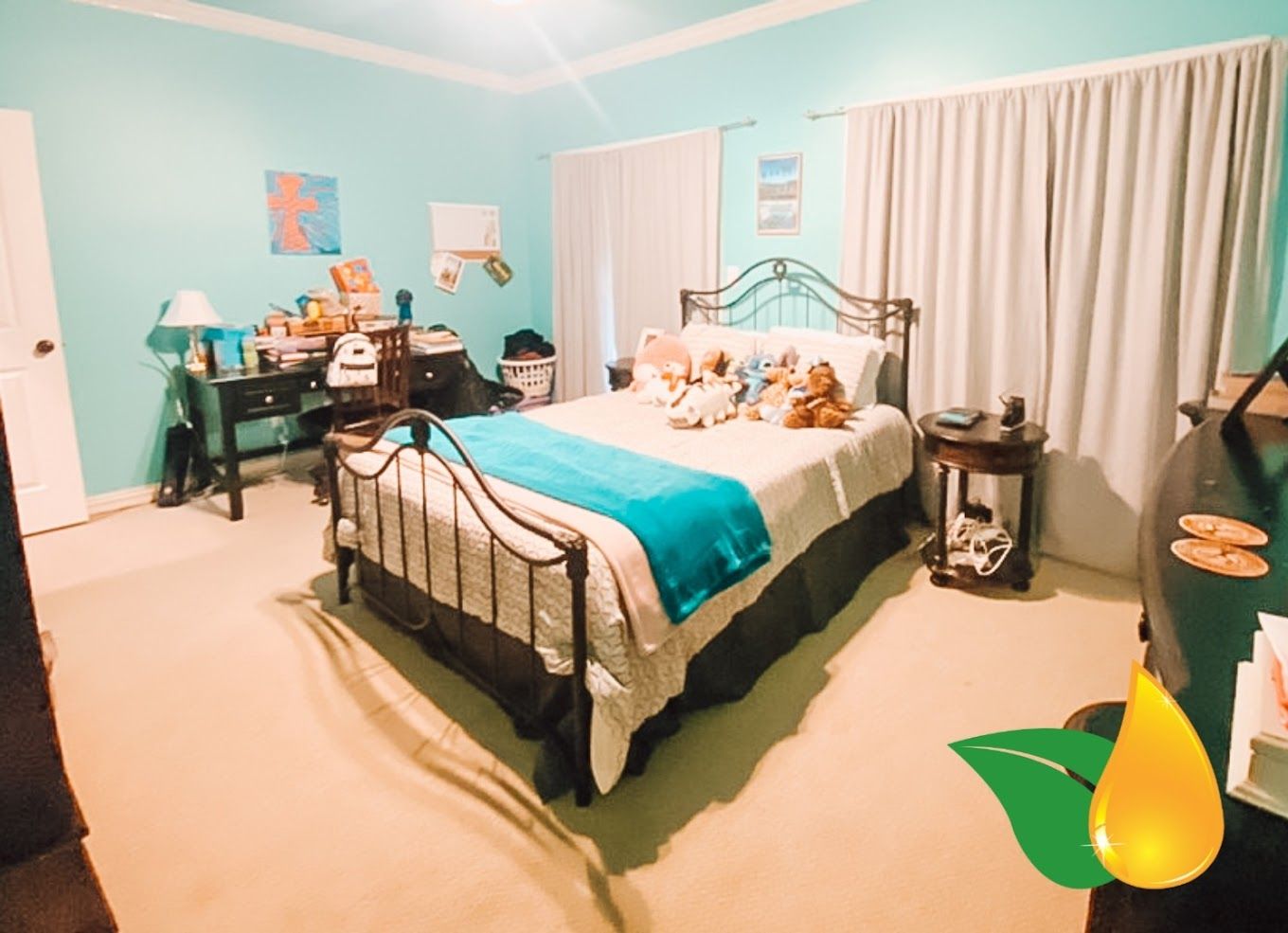 Cozy teal bedroom with black metal bed, desk, curtains, and stuffed animals on the bed