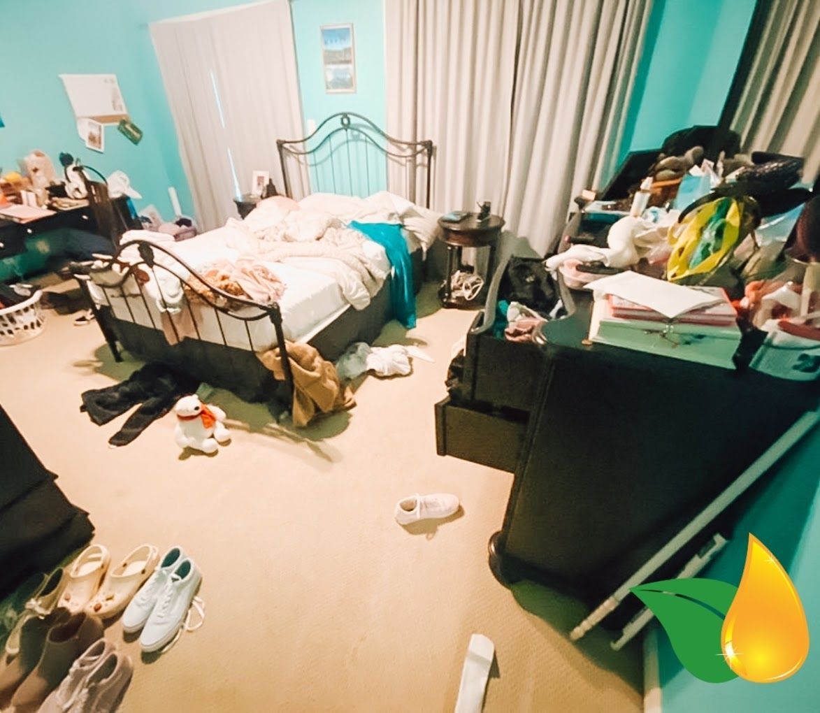 Cluttered bedroom with an unmade bed, clothes and items scattered on the floor and dresser, teal walls and curtains