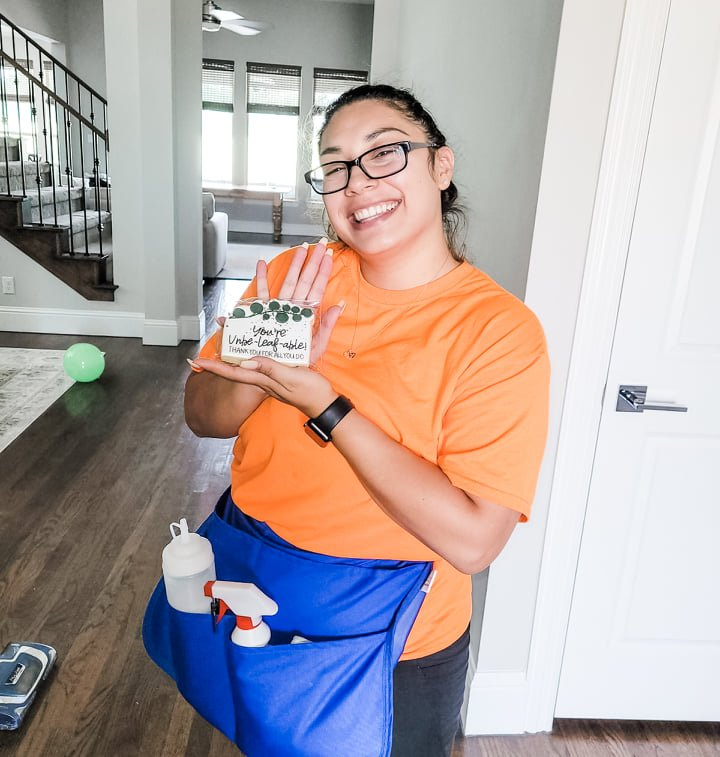 Person in an orange shirt and blue apron smiling and holding a mug in a bright home hallway