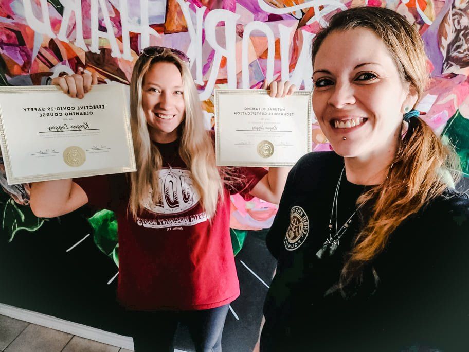 Two smiling people holding certificates in front of a colorful mural