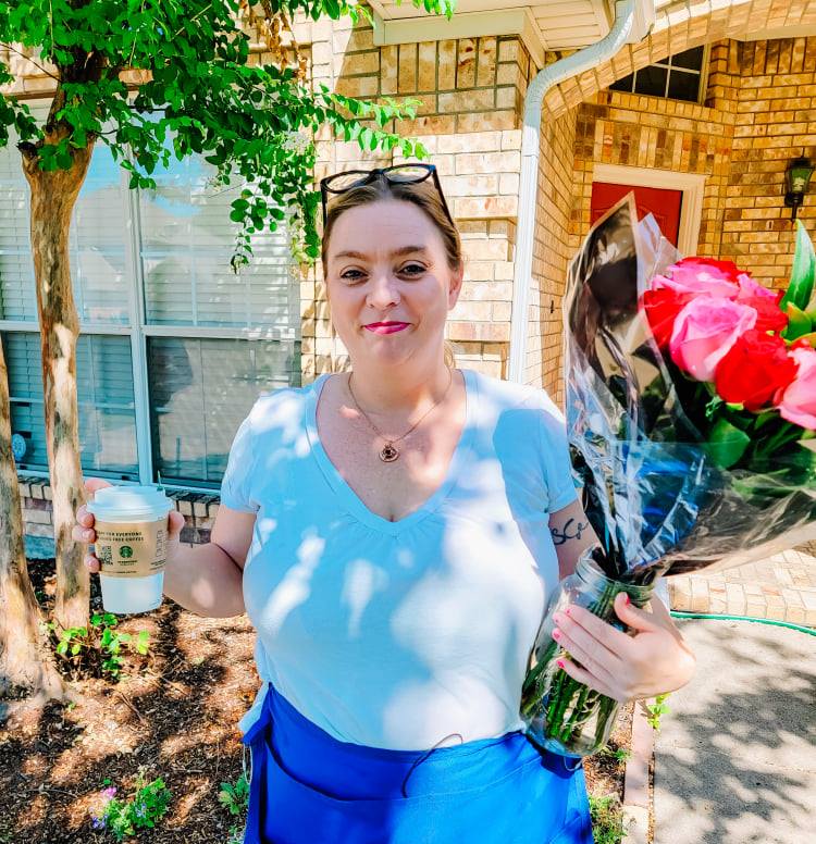 Woman holding a bouquet of red flowers outside a brick house, wearing a light blue top and blue skirt.