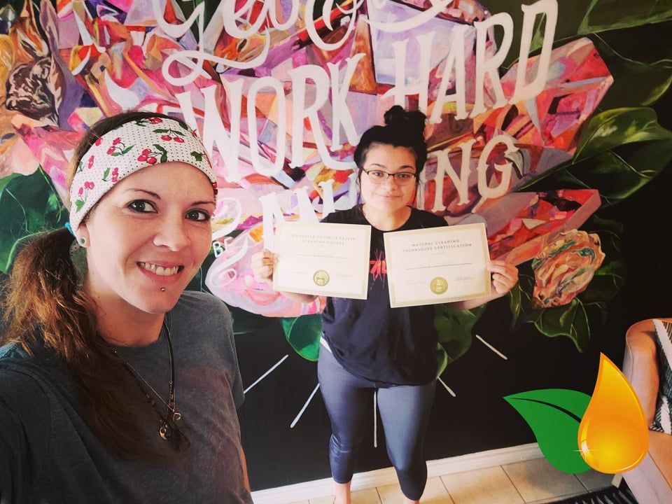 Two women posing with certificates in front of a colorful mural with flowers and large text