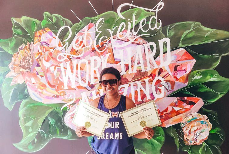 Person holding certificates in front of a colorful floral congratulatory backdrop