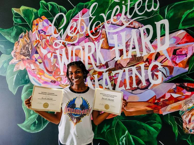 Person holding two awards in front of a colorful mural reading