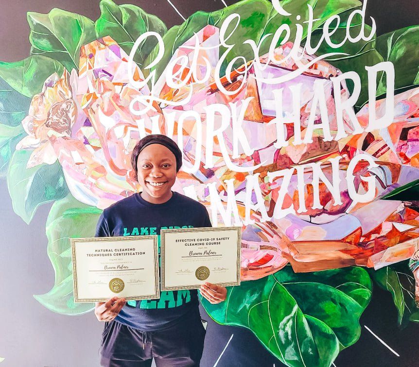 Person holding two certificates in front of a colorful “You’re working hard, amazing” mural
