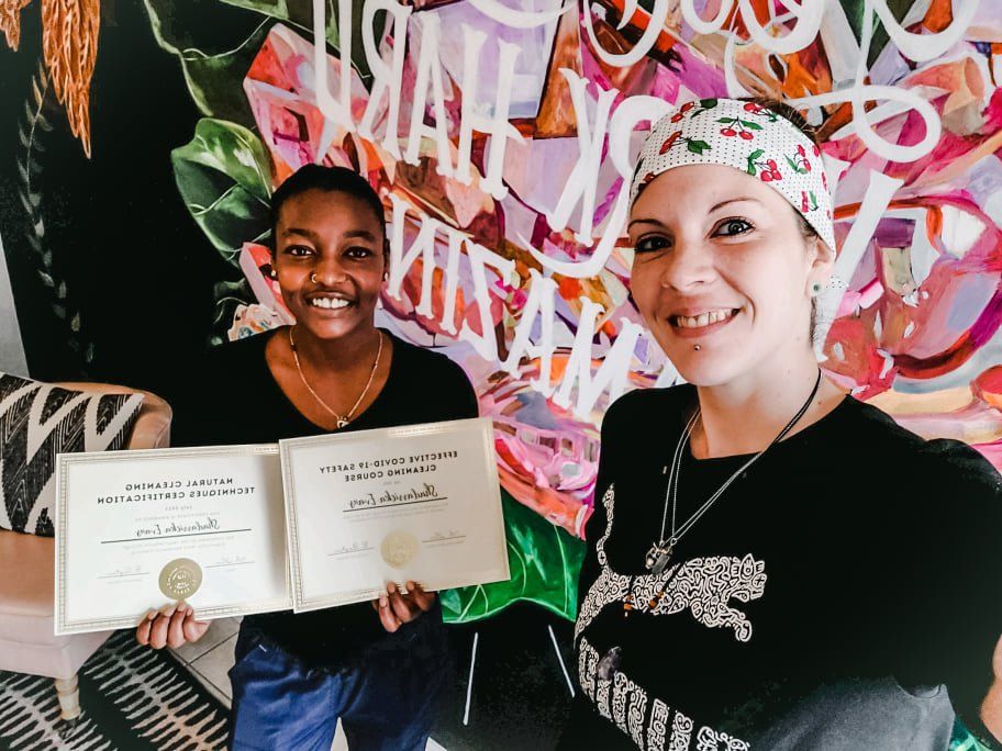 Two people smiling and holding certificates in front of a colorful graffiti wall
