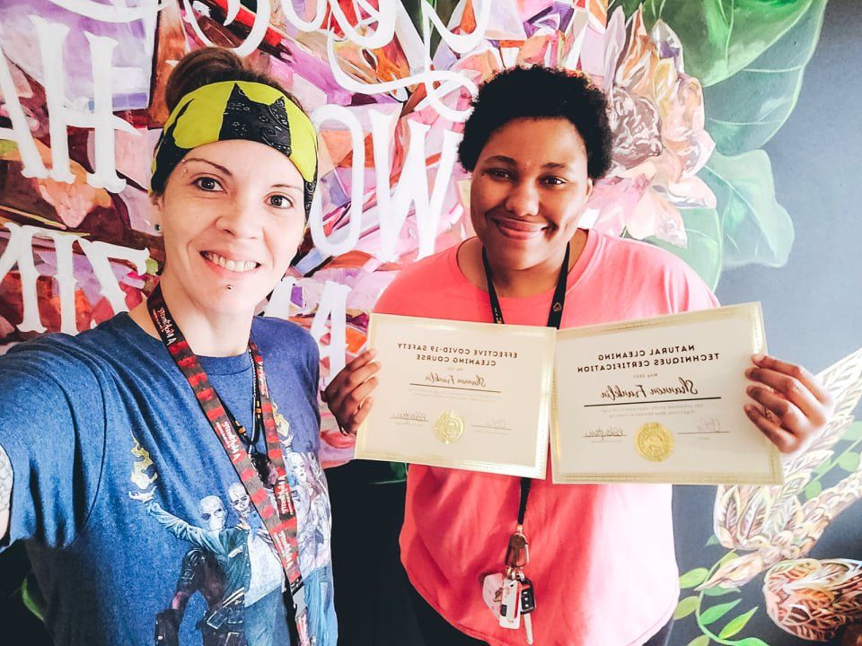 Two people holding certificates and smiling in front of a colorful mural
