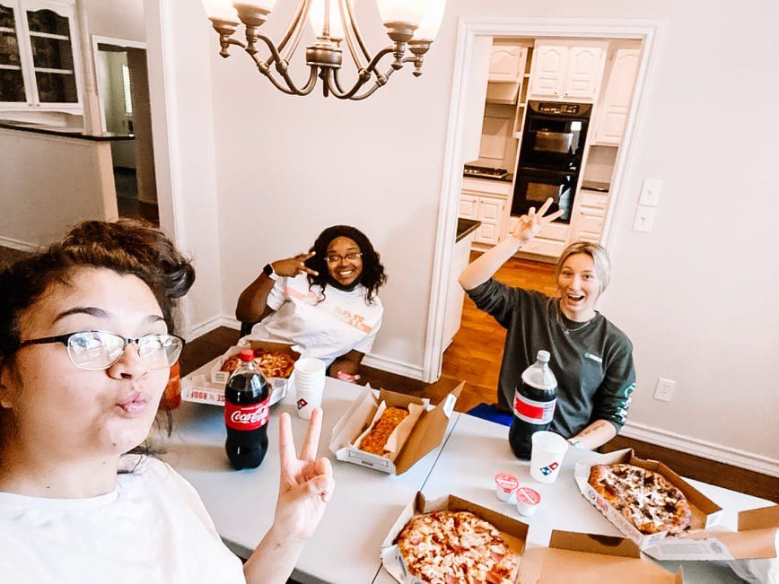 Friends dining around a table, smiling and raising drinks in a bright kitchen-dining room.