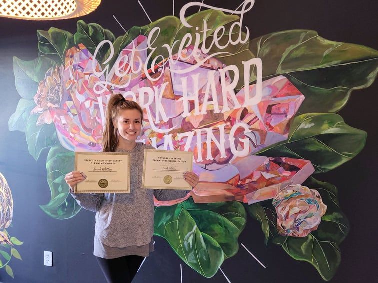 Woman holding two certificates in front of a colorful mural reading “Celebrate hard working”