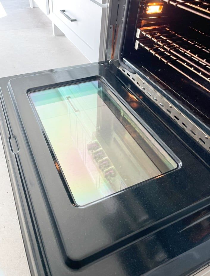 An open black oven door showing a glass window with a rainbow-colored oil-slick effect on the interior surface.