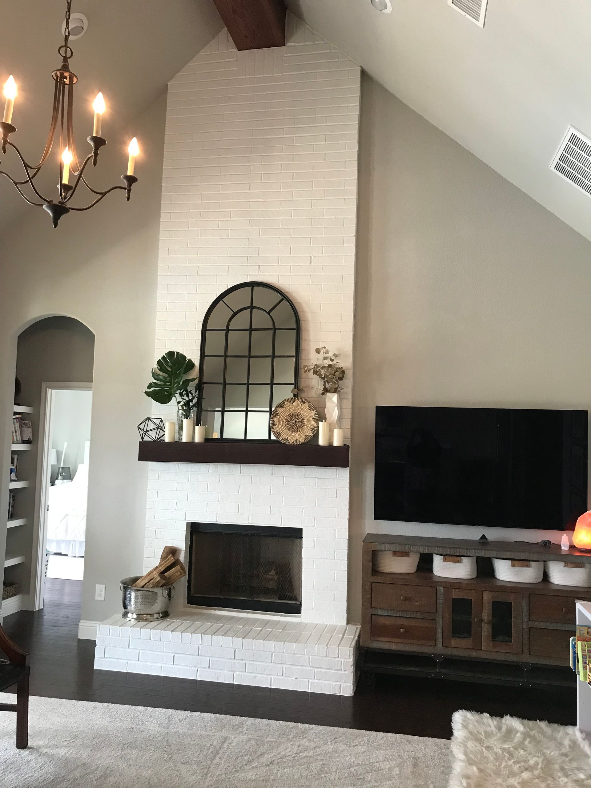 Living room with white brick fireplace, black TV, chandelier, and vaulted ceiling