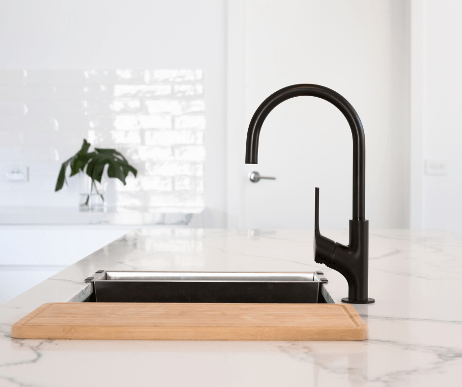 Modern kitchen sink with black gooseneck faucet and wood cutting board on a white marble countertop