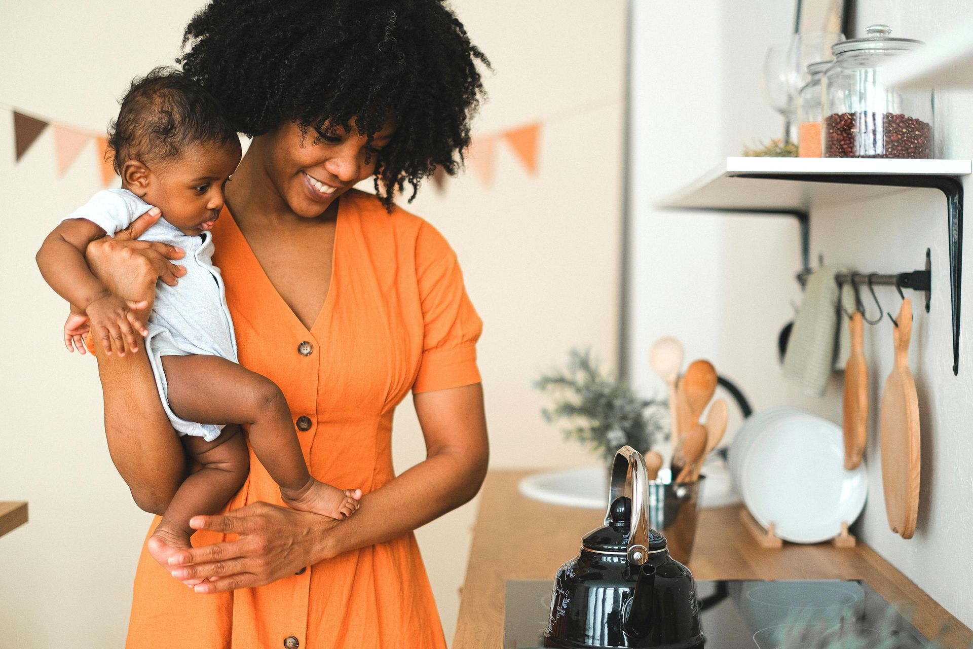 Woman in an orange dress holding a baby in a bright kitchen
