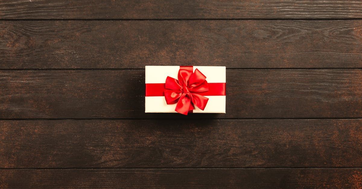 Small white gift box with a red ribbon and bow on a dark wooden surface.