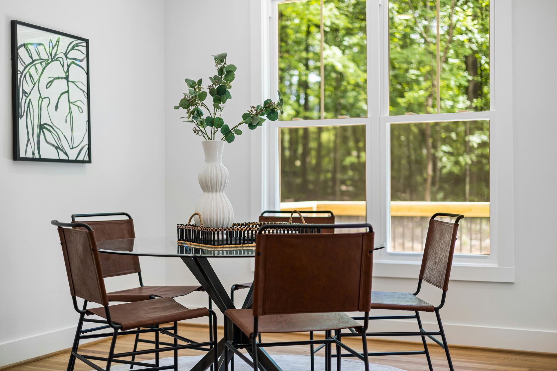 Bright dining nook with a round table, four chairs, vase of flowers, and large window overlooking trees