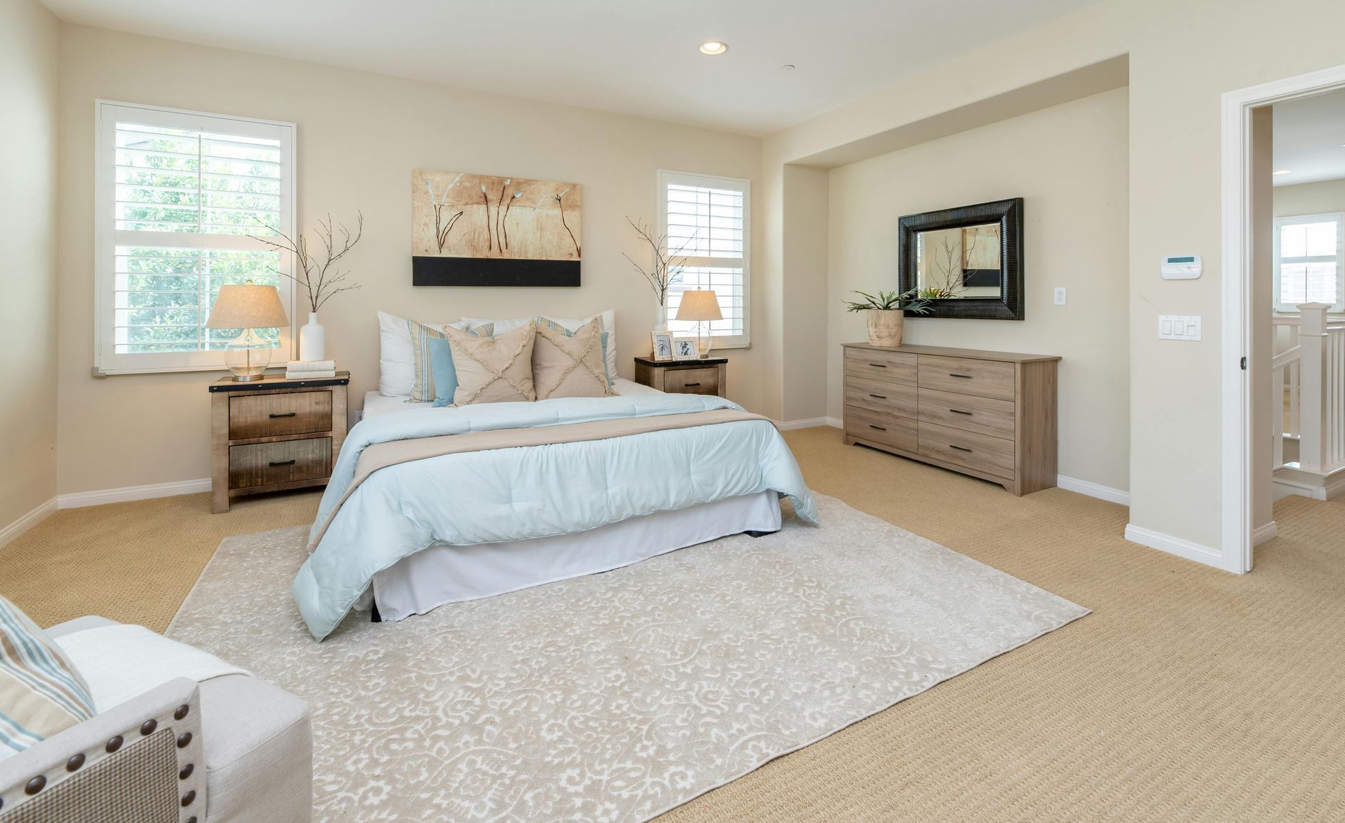 Spacious beige bedroom with a large bed, dresser, mirrors, and two windows on carpeted floor