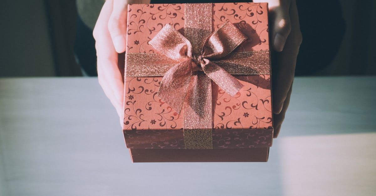 Hands holding a copper gift box with a bow on a table.