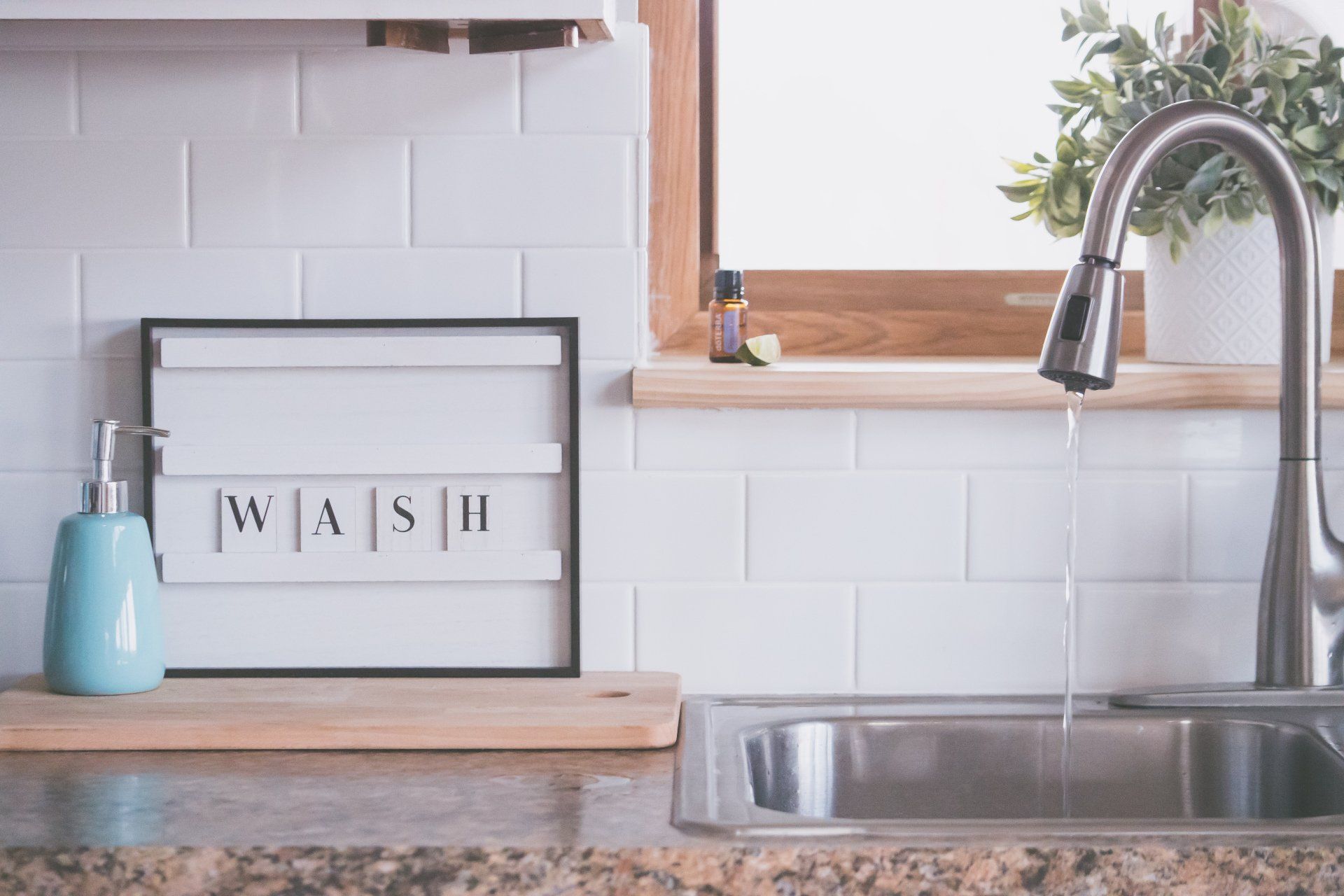 A kitchen sink with a running faucet, a blue soap dispenser, and a sign that says 
