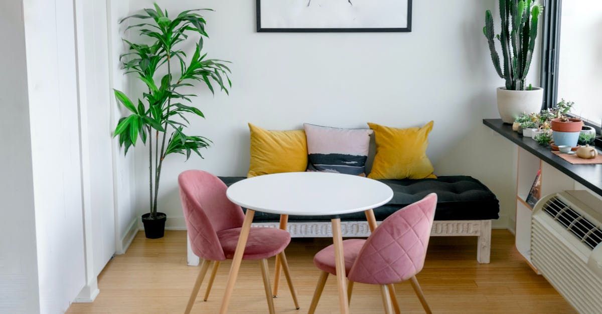 Small modern sitting area with pink chairs, round white table, black sofa, and potted plants
