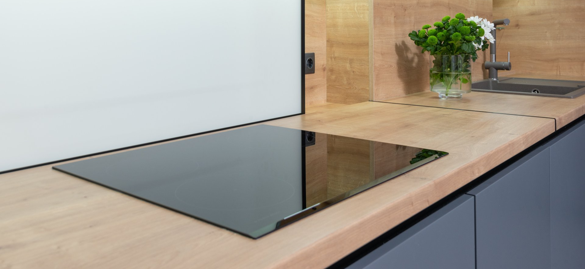 Modern kitchen countertop with black glass induction cooktop and sink near a potted plant