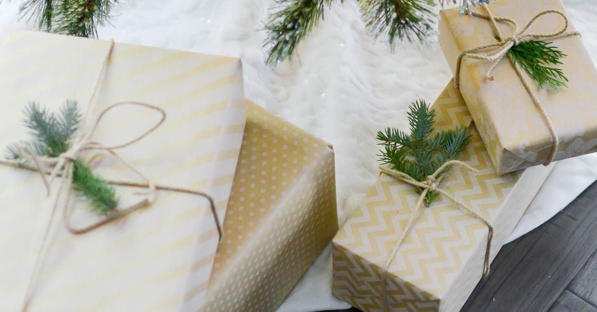 Wrapped holiday gifts with gold ribbon and greenery on a white fur surface