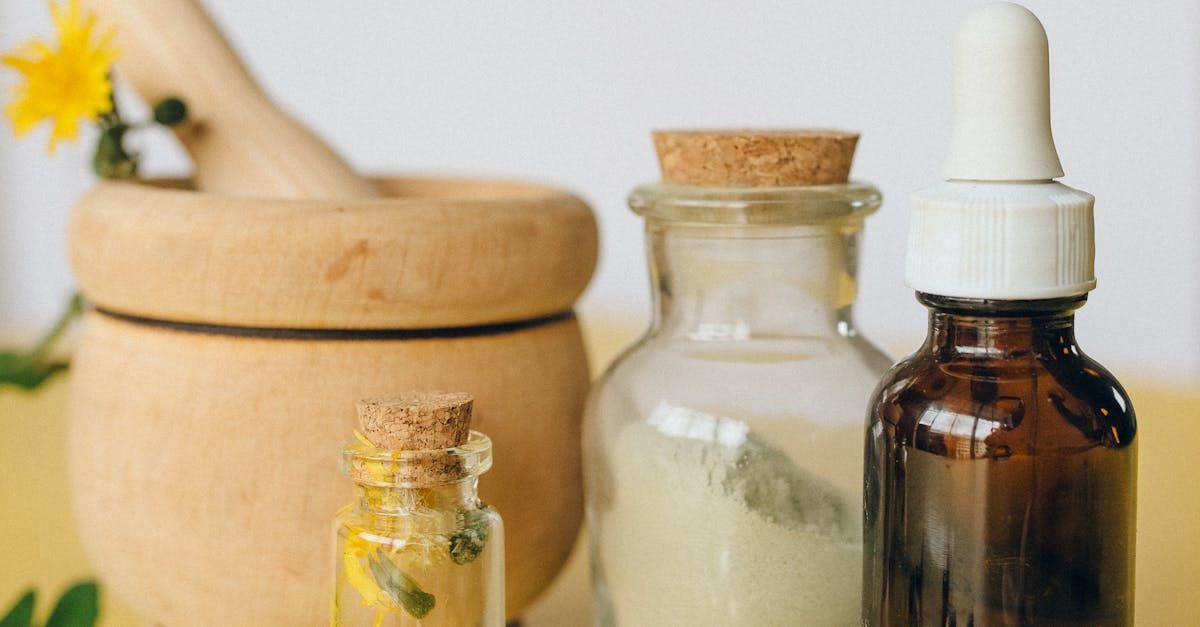A wooden mortar and pestle, a small jar of liquid, a jar of powder, and an amber glass dropper bottle on a yellow surface.
