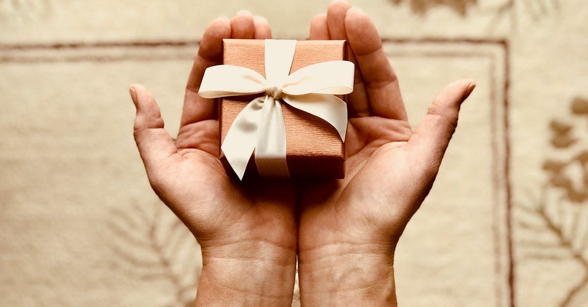 Hands holding a small wrapped gift with a cream ribbon on a wooden background