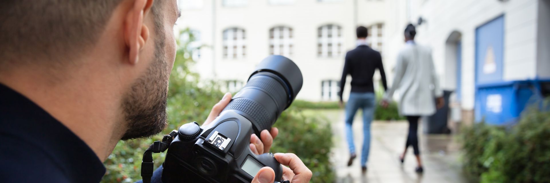 A man is taking a picture of a couple walking down a sidewalk with a camera.