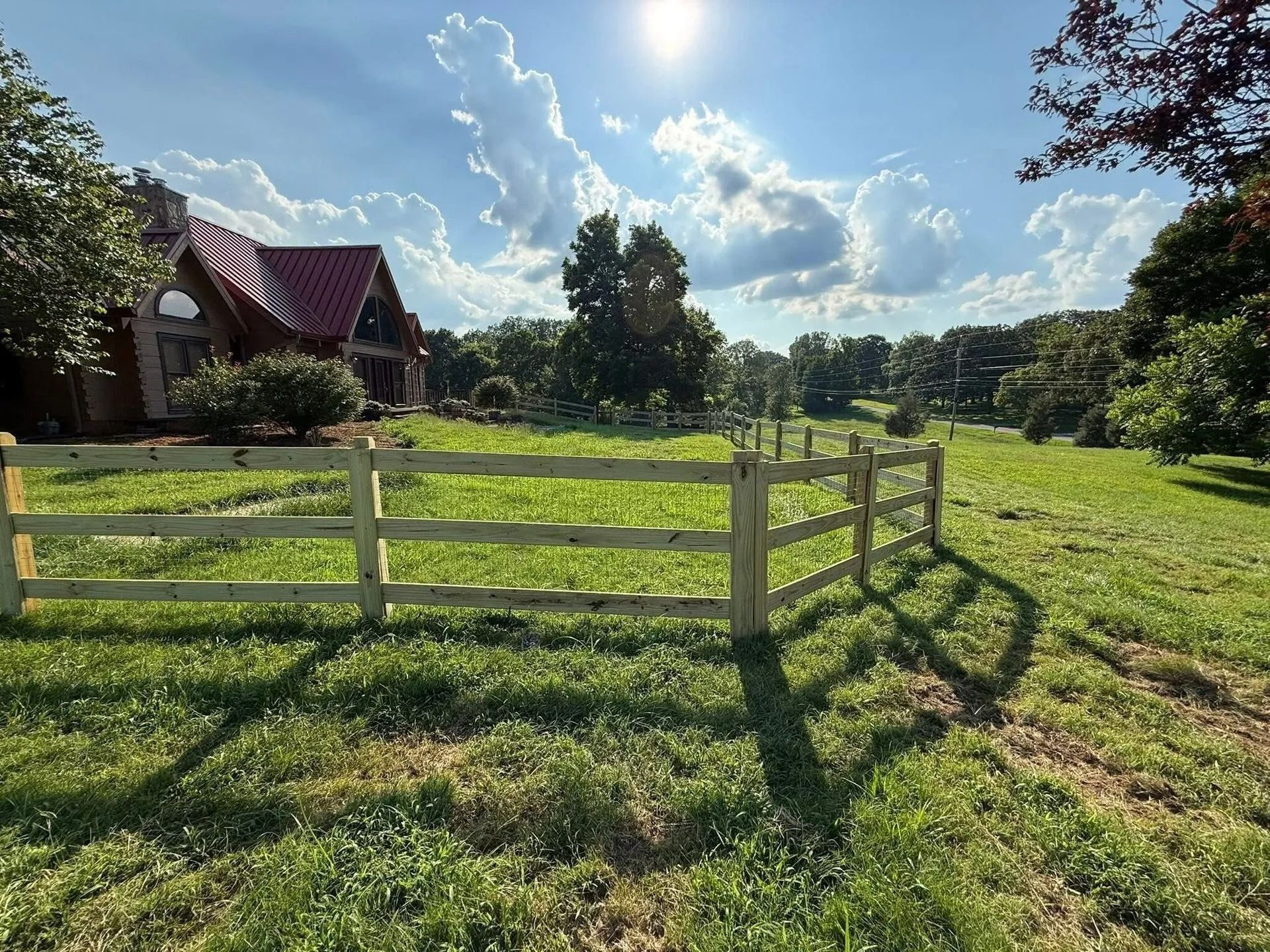Wooden fence in a sunny field with a house visible in the background.