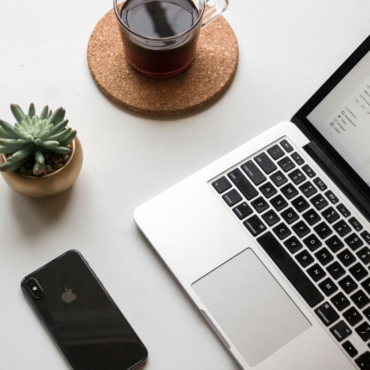 A person is typing on a laptop while holding a cell phone.