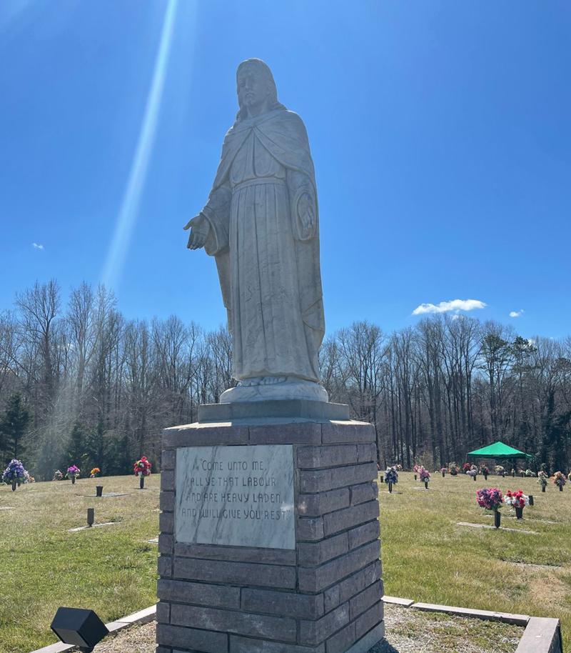 There is a statue of jesus in the middle of a cemetery.