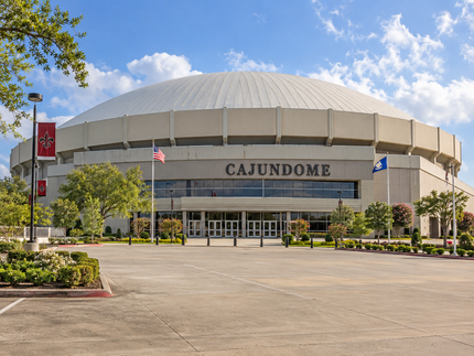 Cajundome arena entrance with dome roof, flags, and empty parking lot under a sunny sky