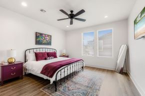 Bright bedroom with white walls, magenta bedding, a black metal bed frame, and two windows with blinds