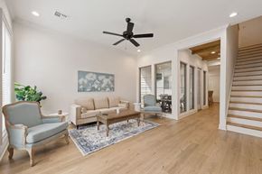 Bright modern living room with beige sofa, blue armchair, coffee table, ceiling fan, and wooden floors