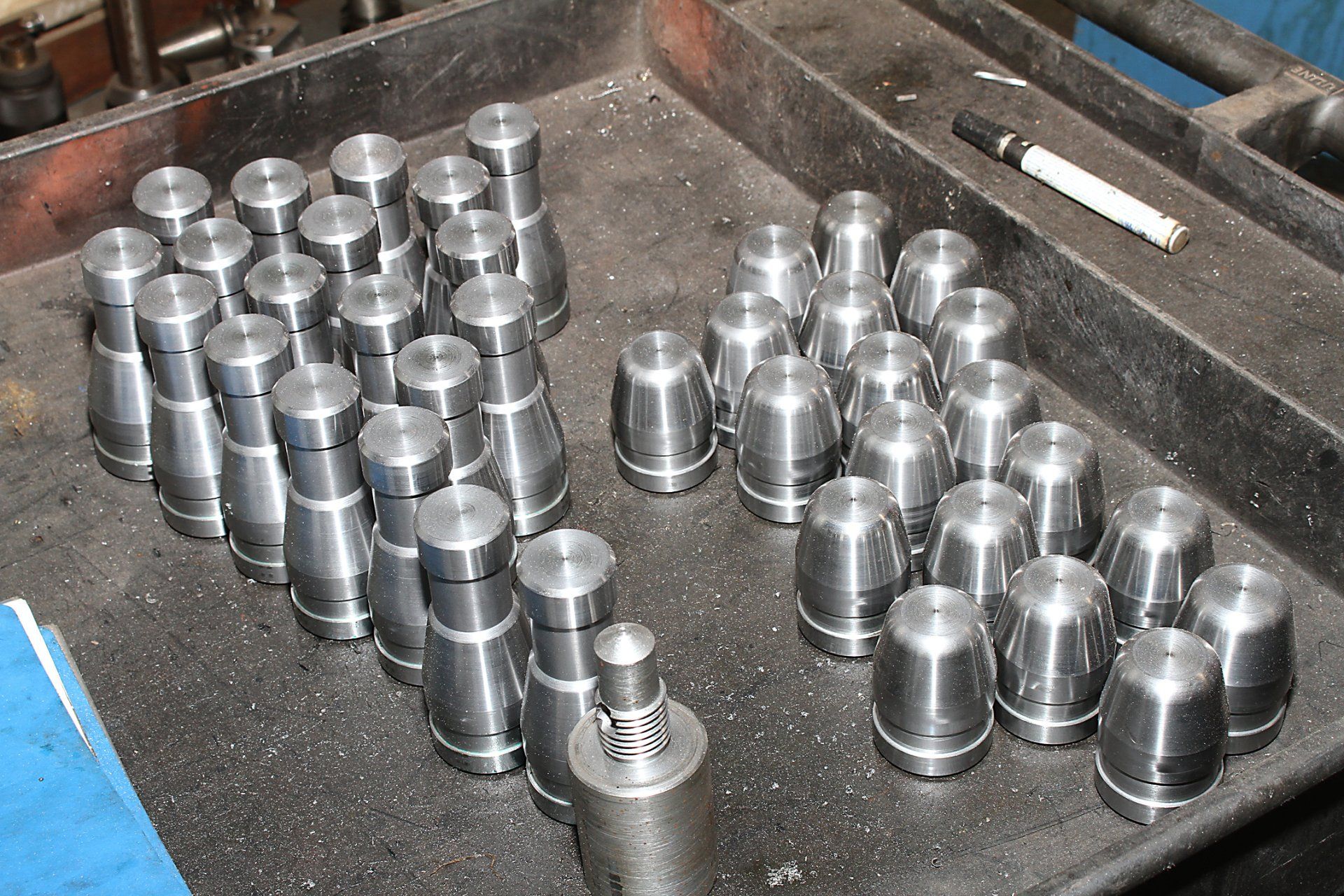 Metal machined parts arranged in a tray, a pen lies beside them.