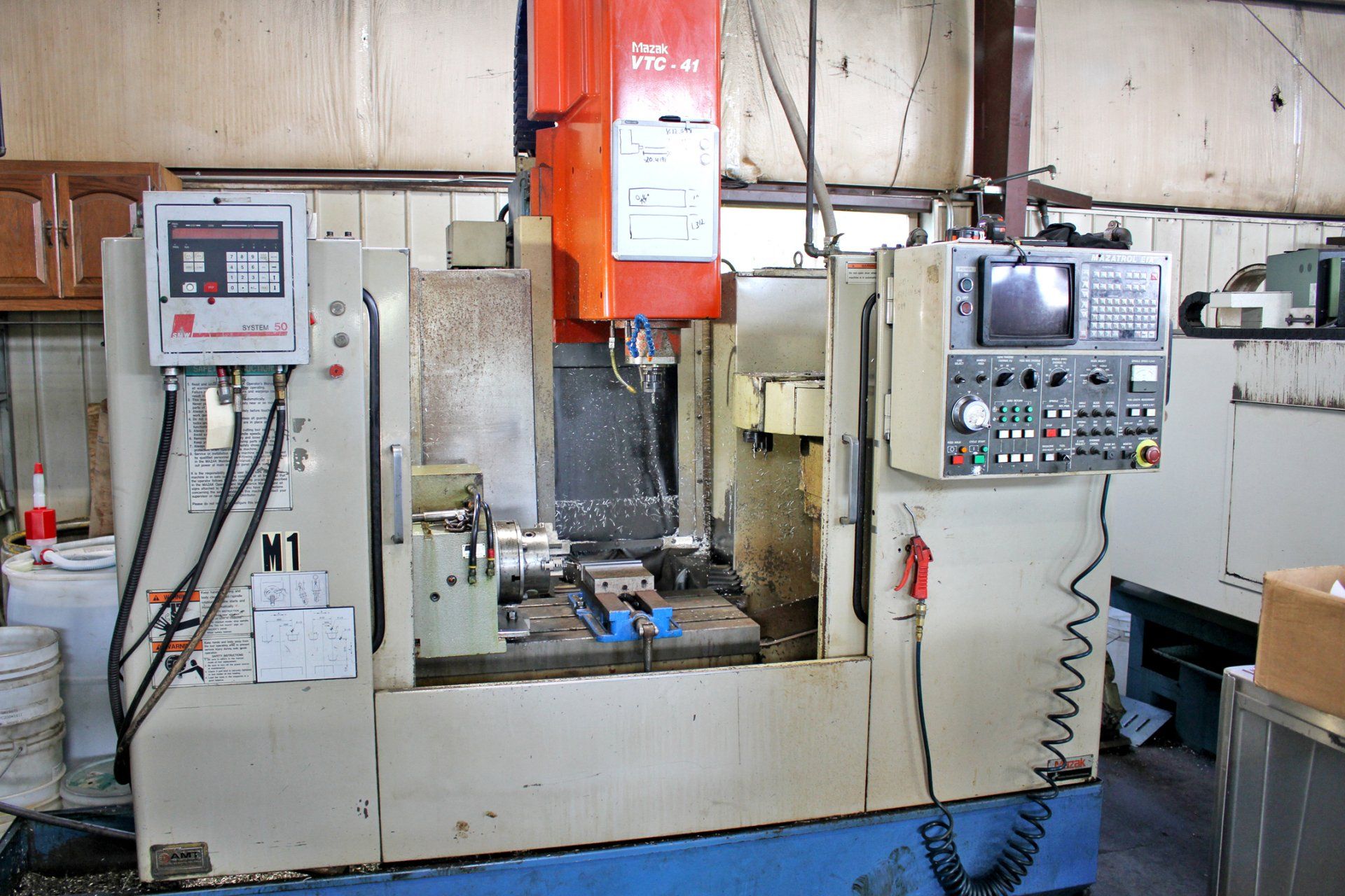 CNC milling machine in a workshop, beige and orange, with control panels and a work area.