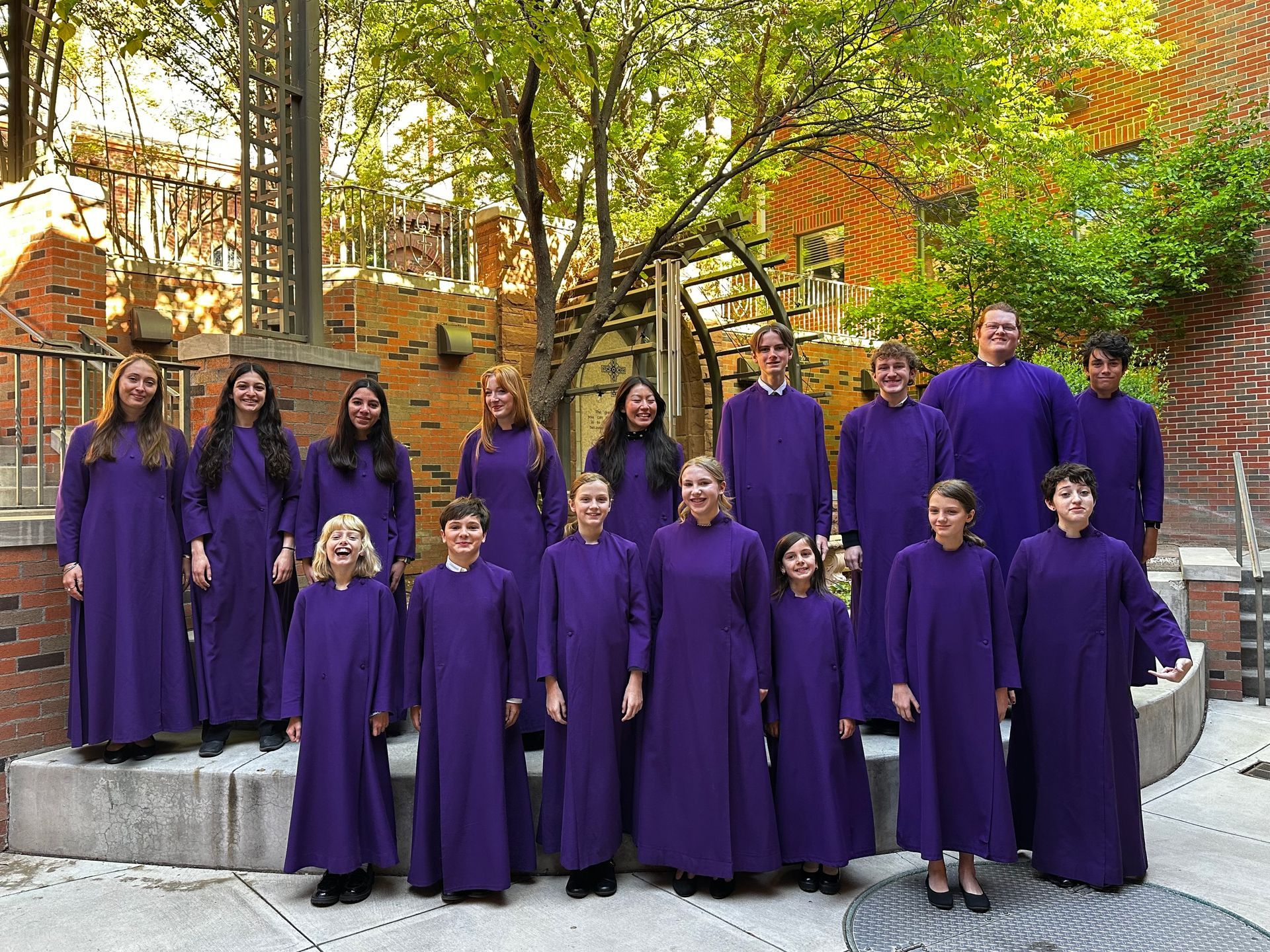 Cathedral of St John's Choir in purple robes posing outdoors on a stone terrace with trees and brick buildings behind them