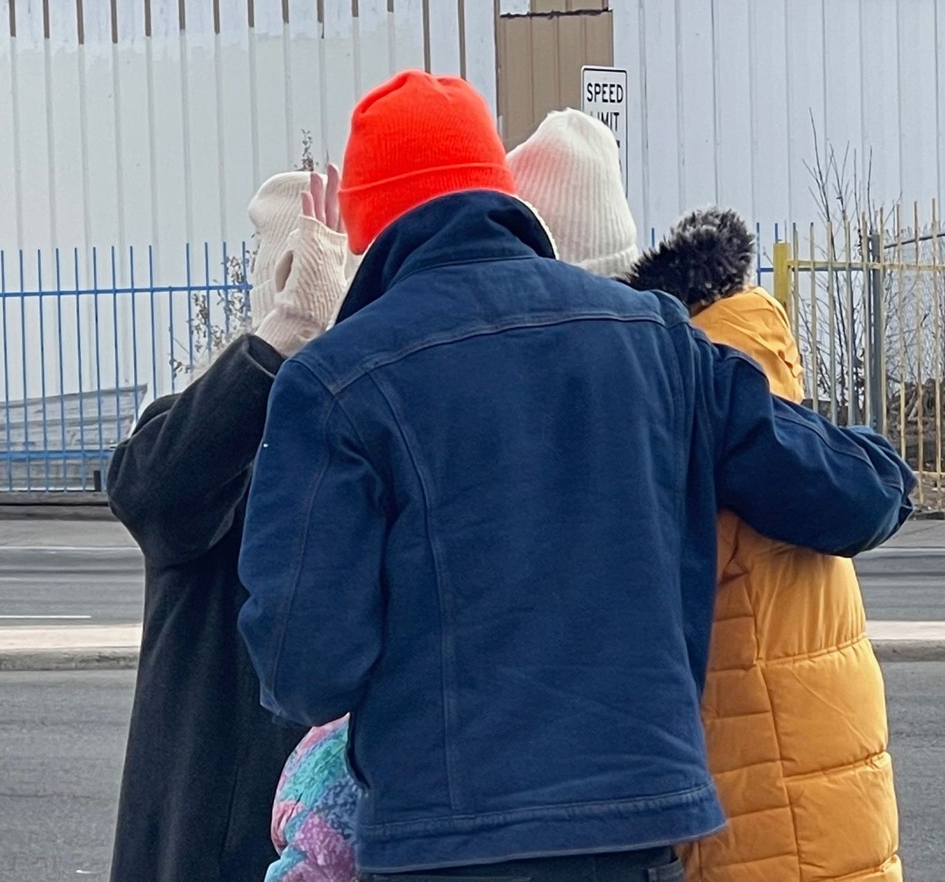 Three people in winter coats and hats stand outdoors praying