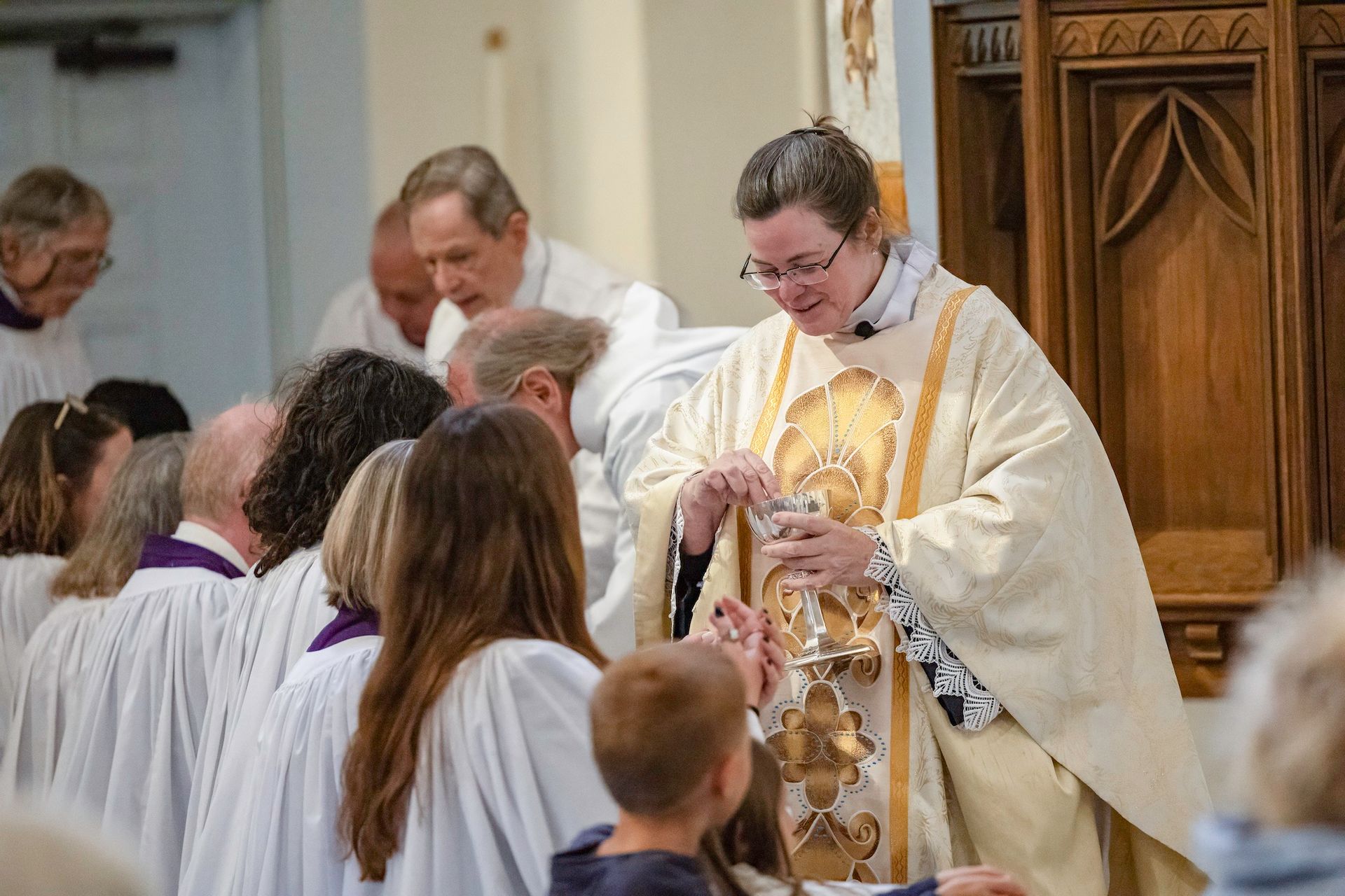Priest in white and gold vestments distributes communion to a church congregation